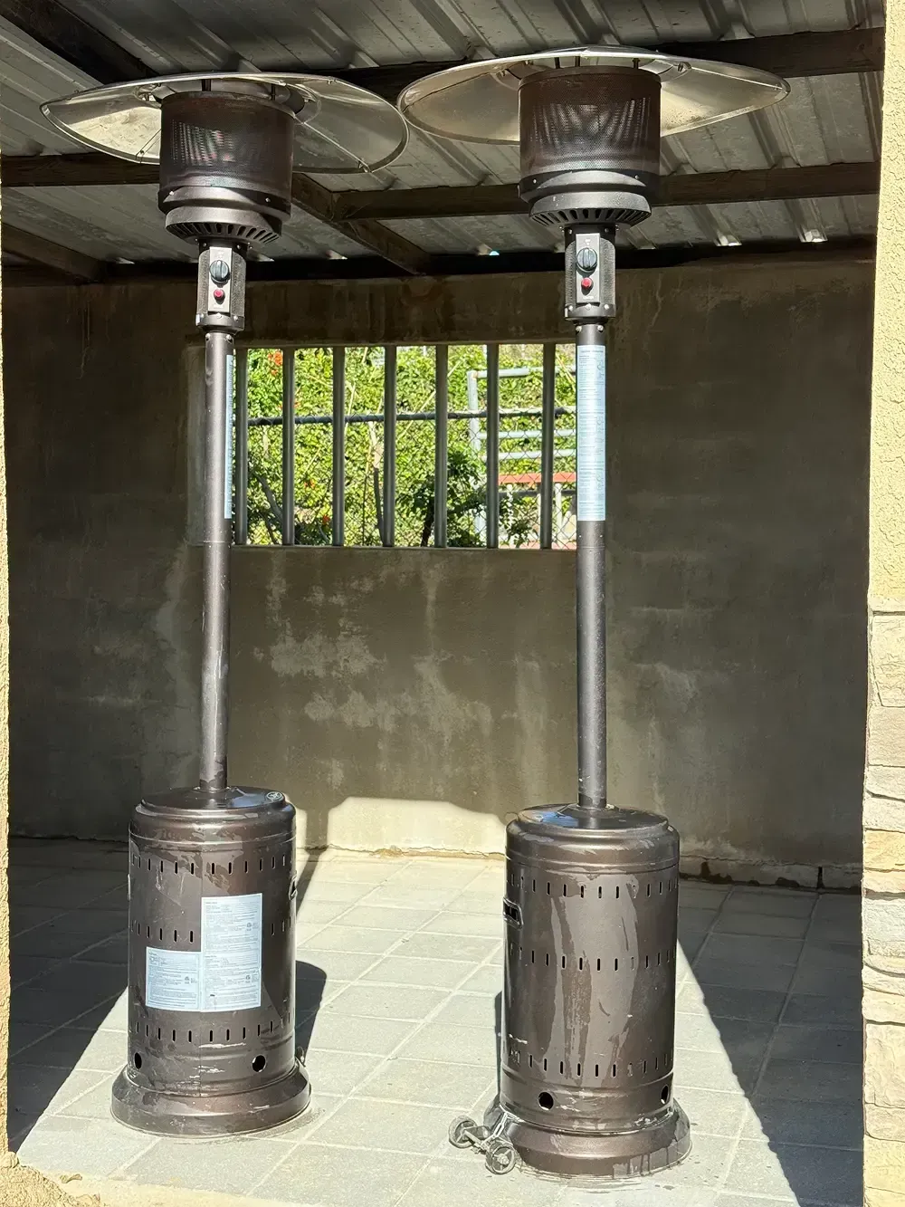 Two outdoor patio heaters standing on a concrete surface, under a canopy.