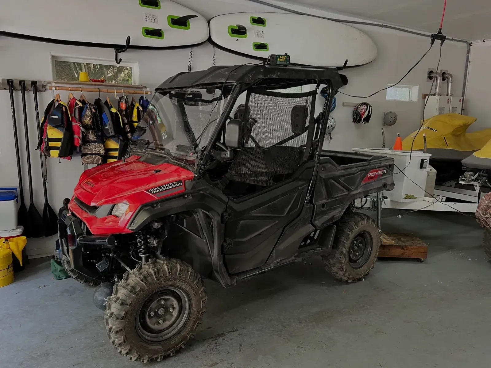 Red and black Honda side-by-side vehicle in a garage with paddle boards and life vests.