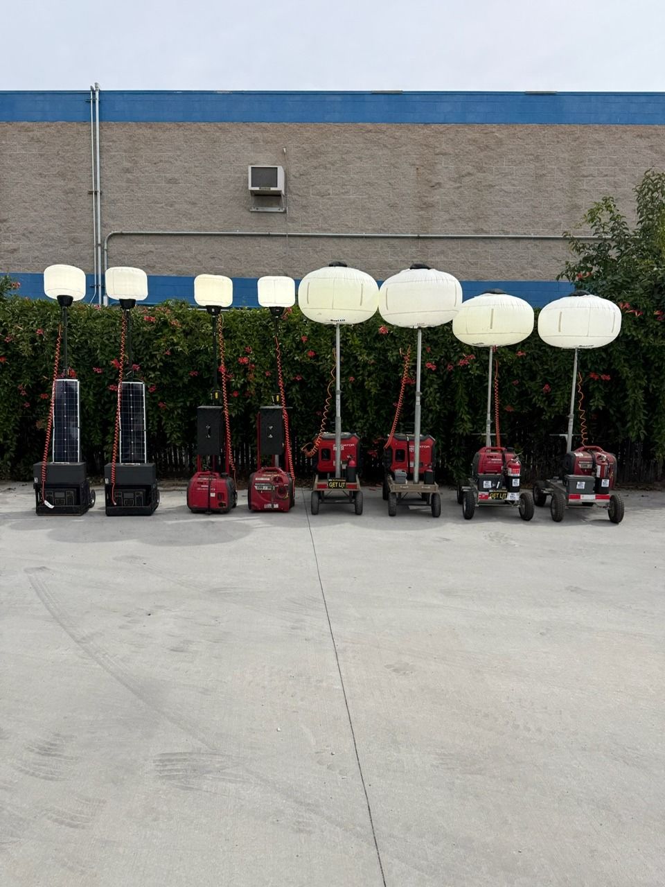 Line of portable lighting units on a concrete surface, against a blue brick wall.