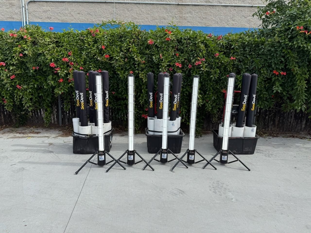 Fireworks display setup with black tubes and launch stands in front of a hedge.