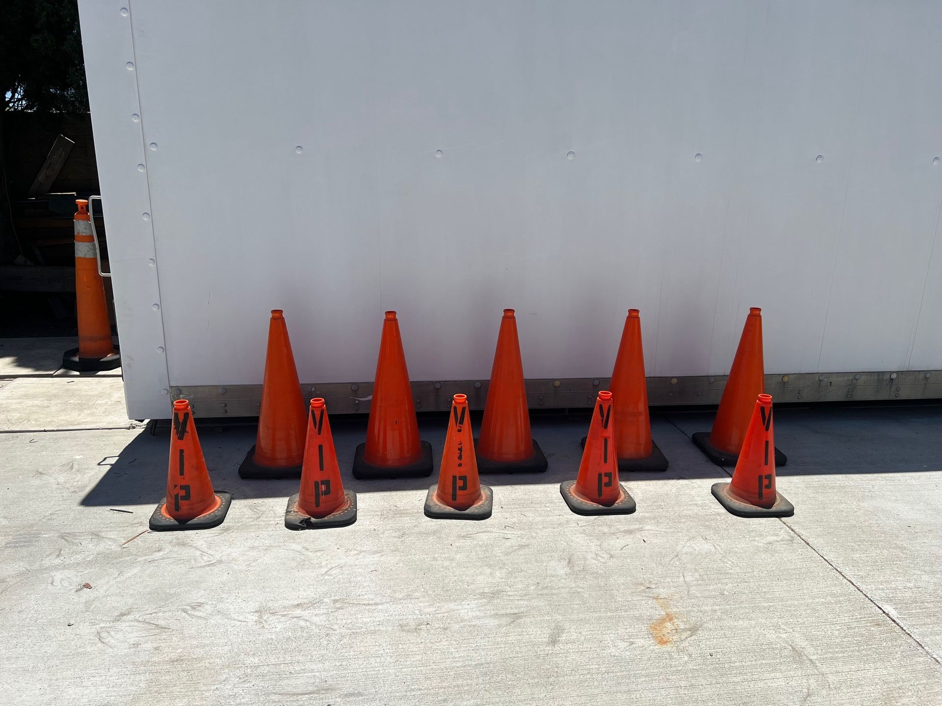 Ten orange traffic cones lined up in front of a white wall, 
