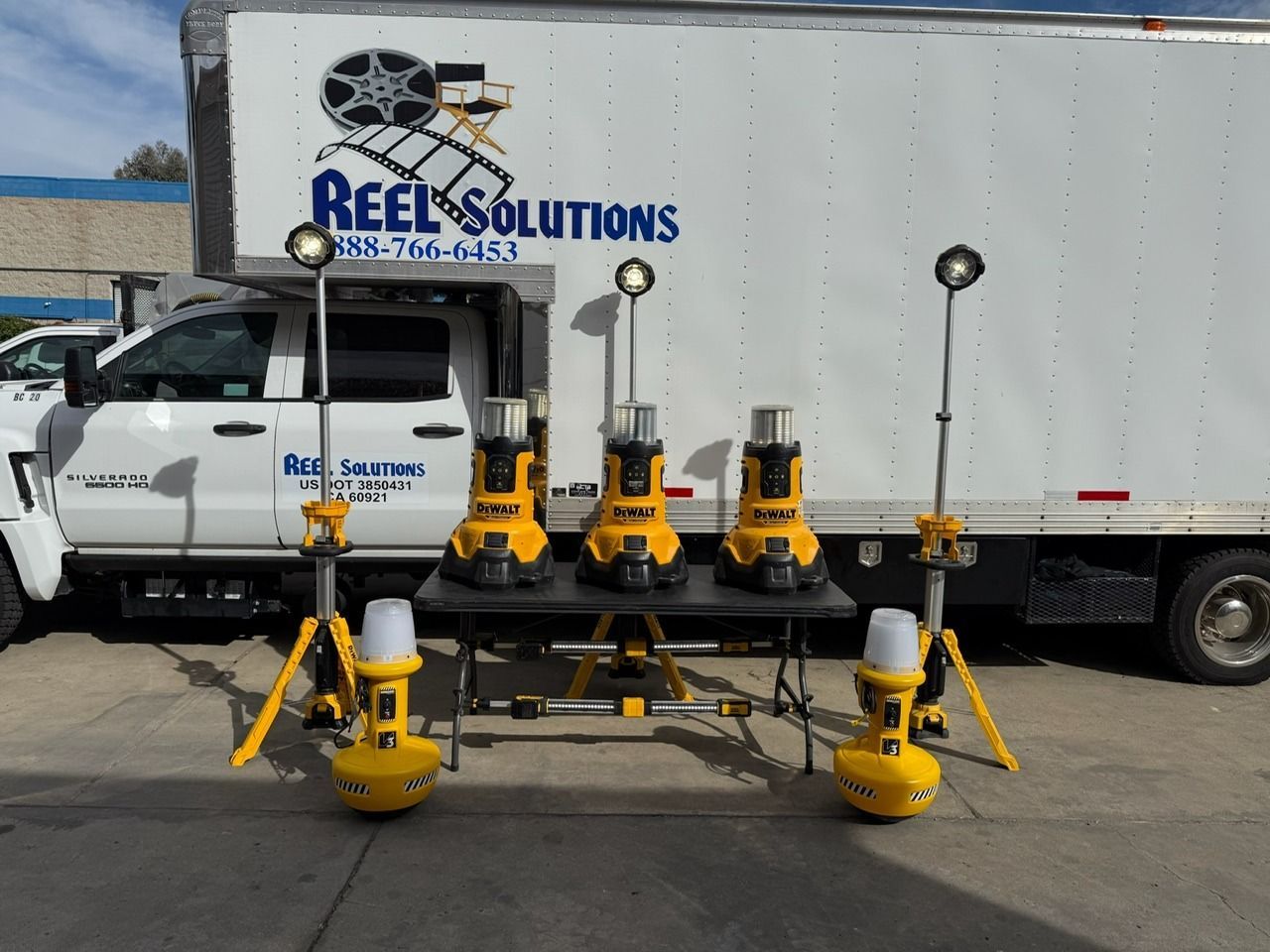 Five yellow work lights on tripods in front of a white truck with 