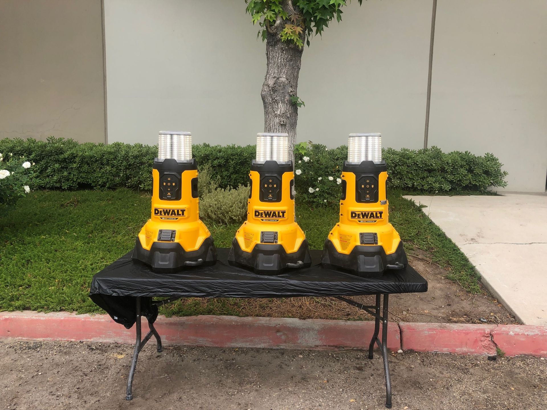Three yellow and black DeWalt work lights on a table outdoors in front of a building.