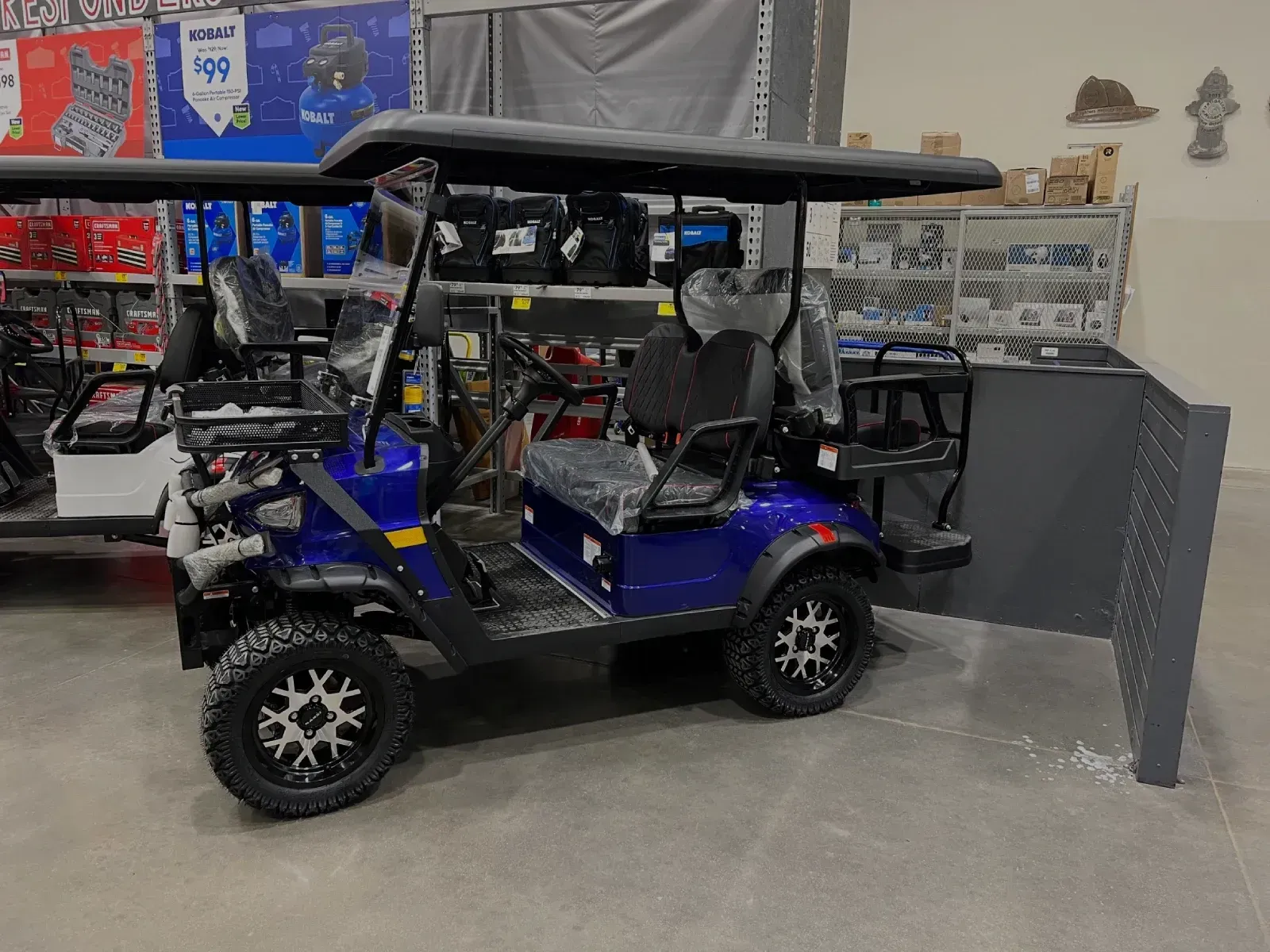 Blue golf cart with black roof and wheels, inside a store.