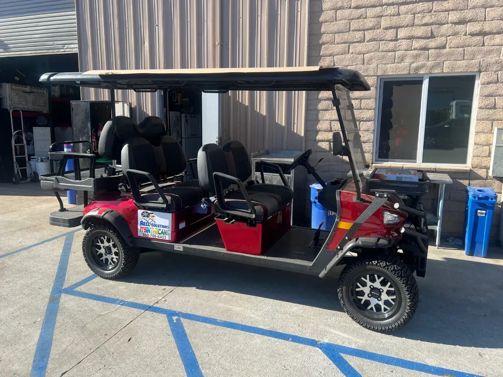 Red six-person golf cart parked outside a building on a sunny day.