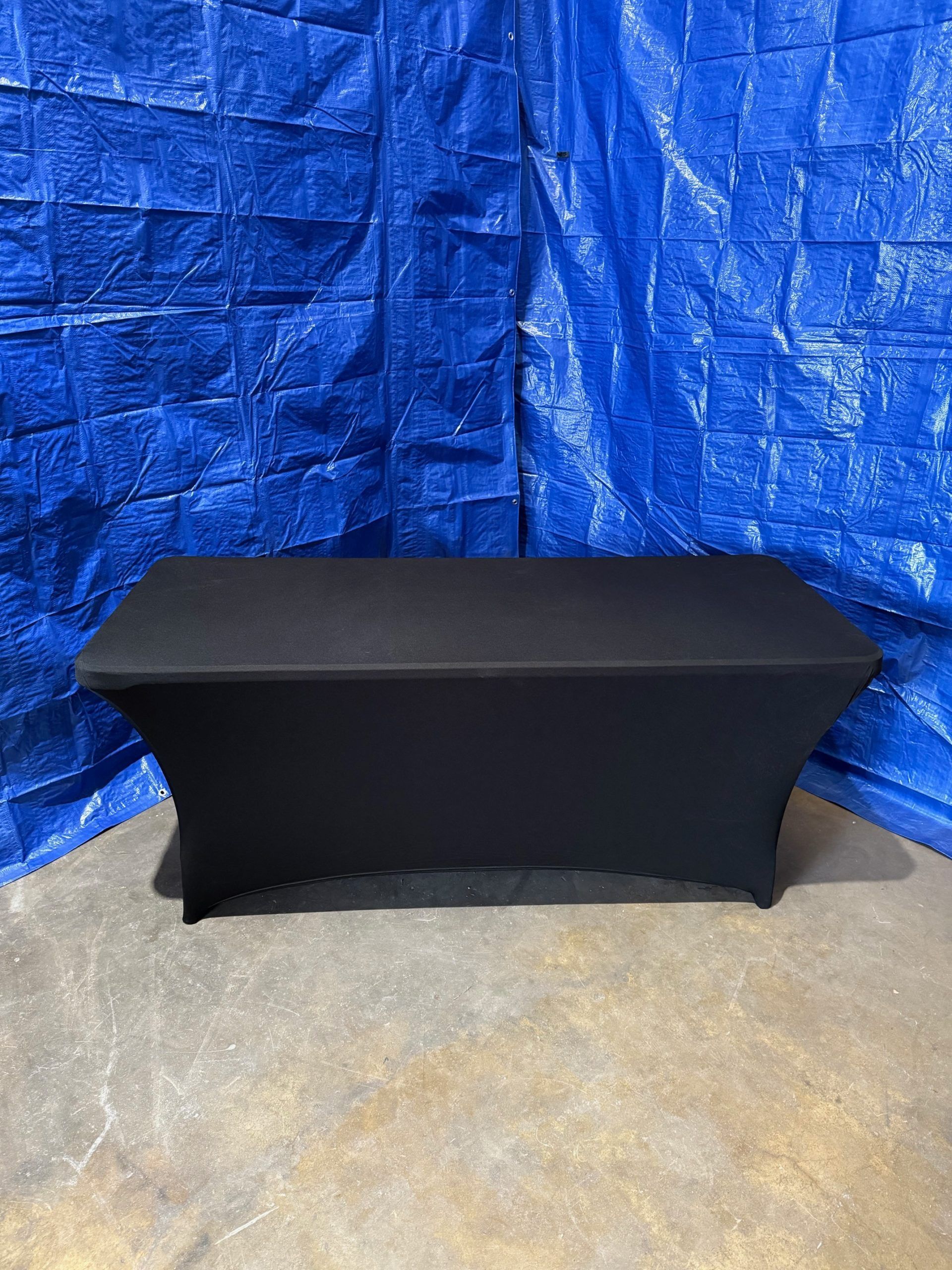 Black table draped in a black cover against a blue tarp backdrop.