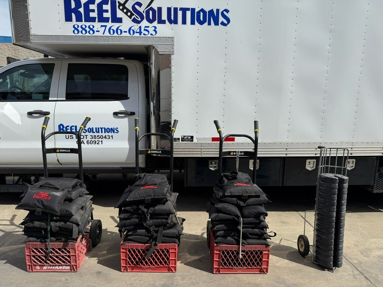 Three carts of sandbags and a roll of gray mats next to a truck. 