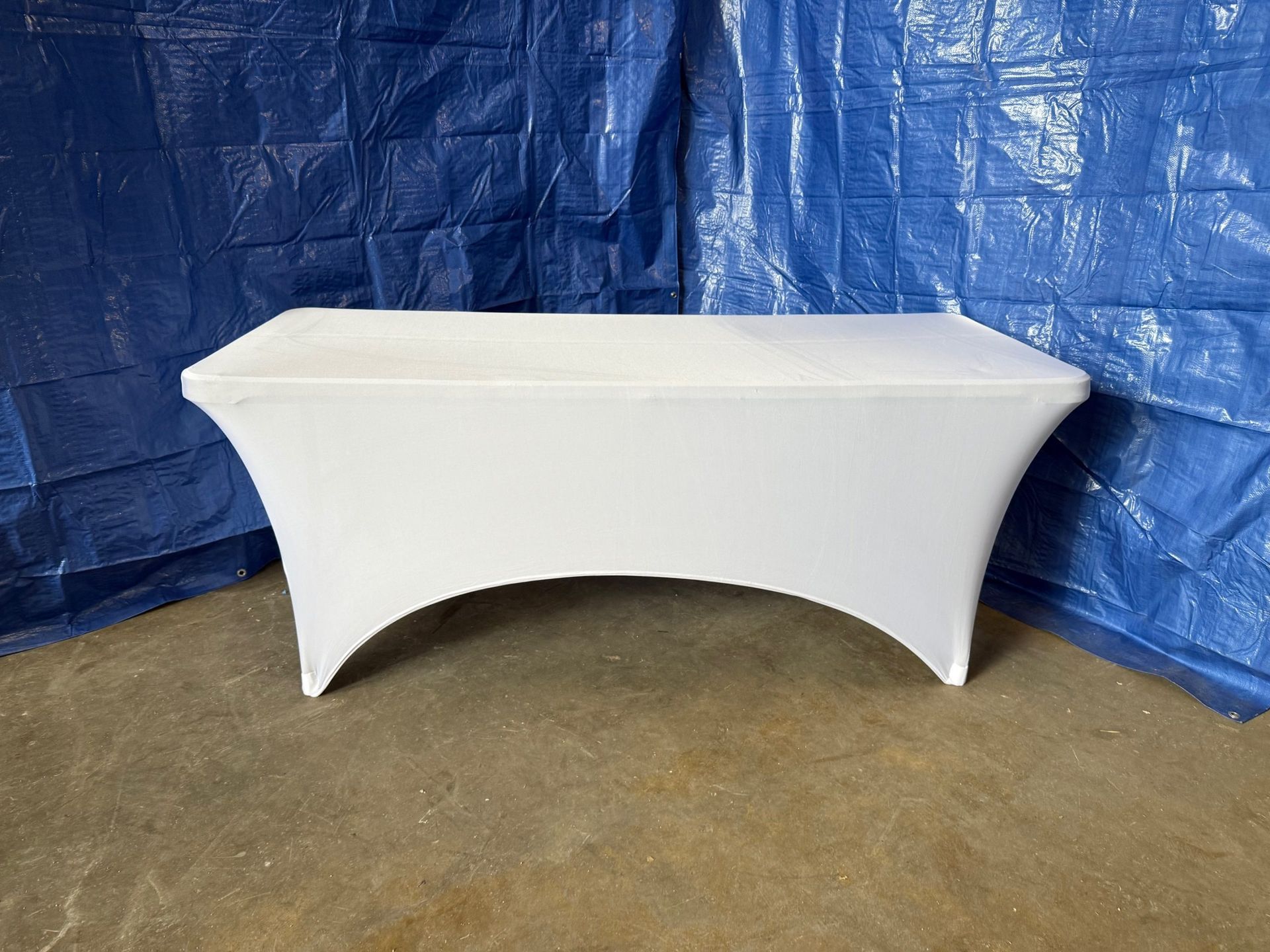 White stretch table cover on a rectangular table against a blue tarp backdrop.