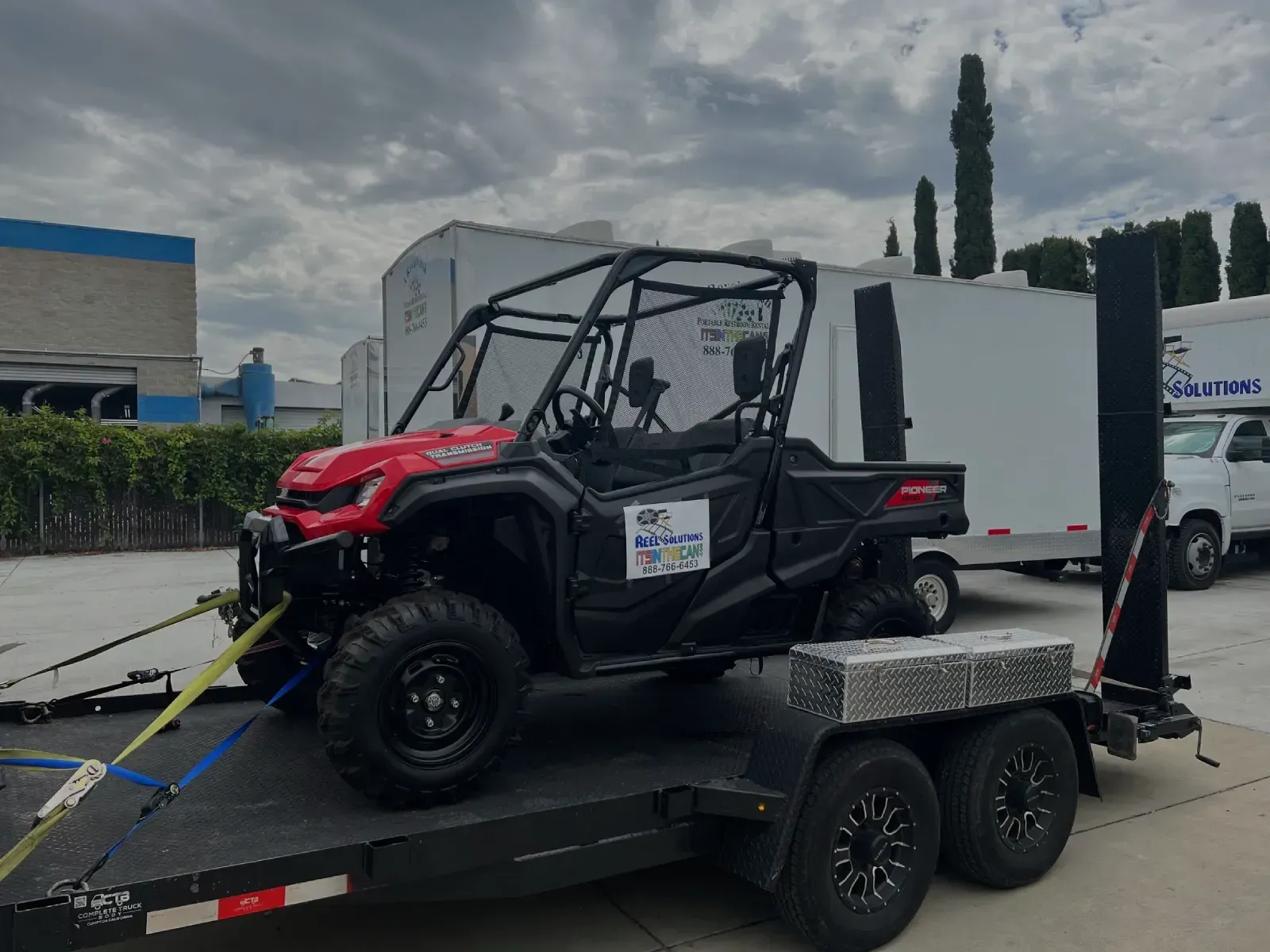 Red and black Honda side-by-side vehicle on a trailer, secured with straps, parked outside.