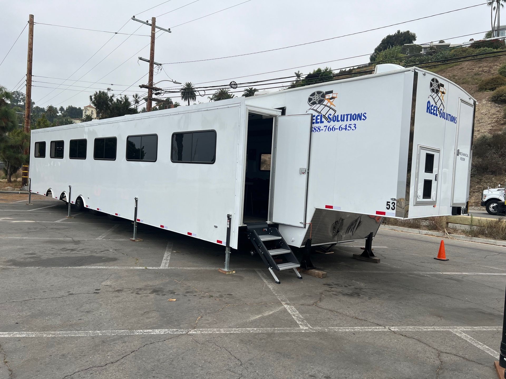 White trailer with side entrance, steps, and windows on asphalt. Blue text on side. Cloudy sky.