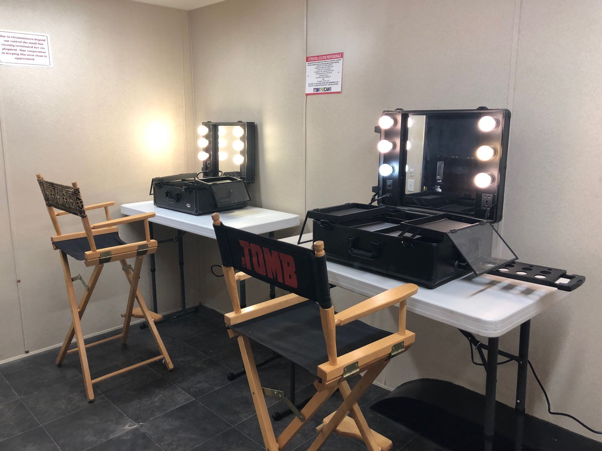 Two makeup stations with lighted mirrors, folding tables, and director's chairs in a room.