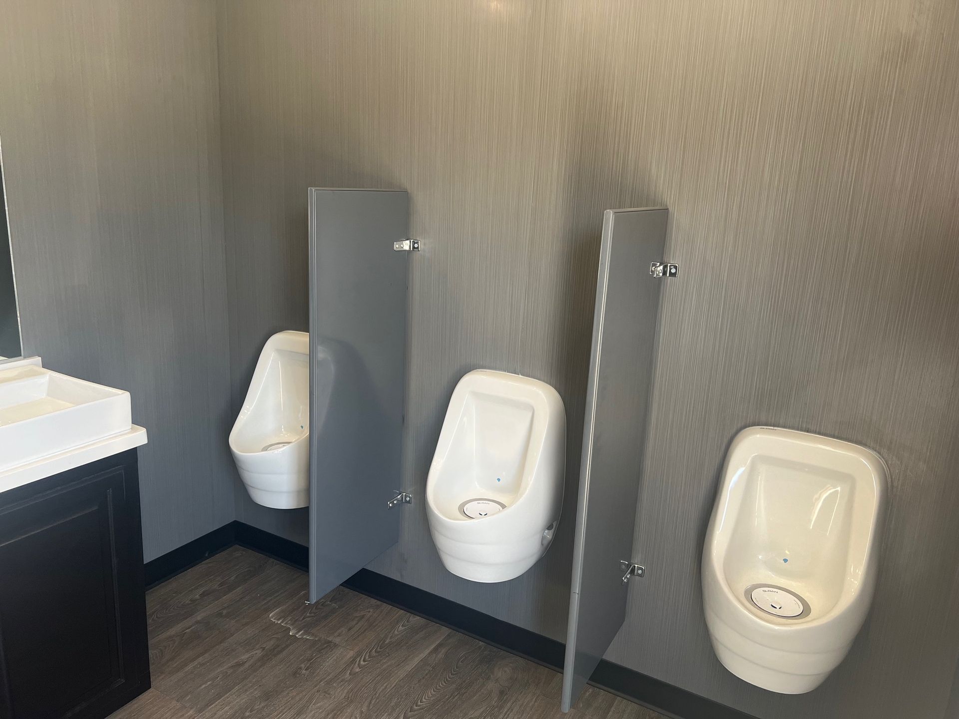 Three urinals in a public restroom with grey dividers and walls.