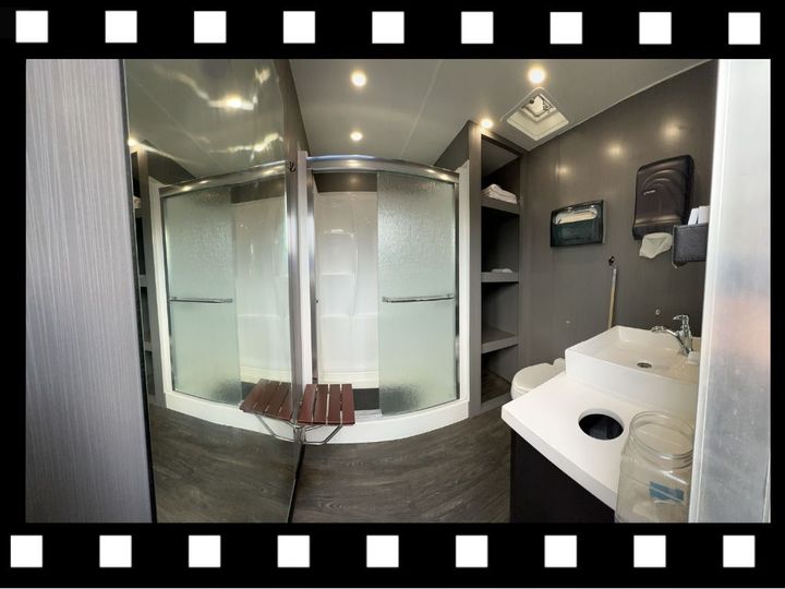 Bathroom with a large, glass-enclosed shower, a sink, and a shelf unit. Gray and white color scheme.