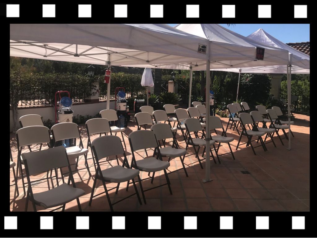 Rows of white chairs under white tents on a patio, prepared for an event.
