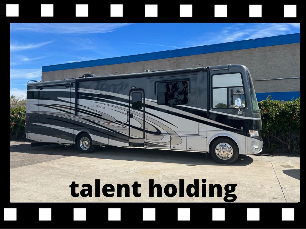 Large, silver and black RV parked outside a building on a sunny day.