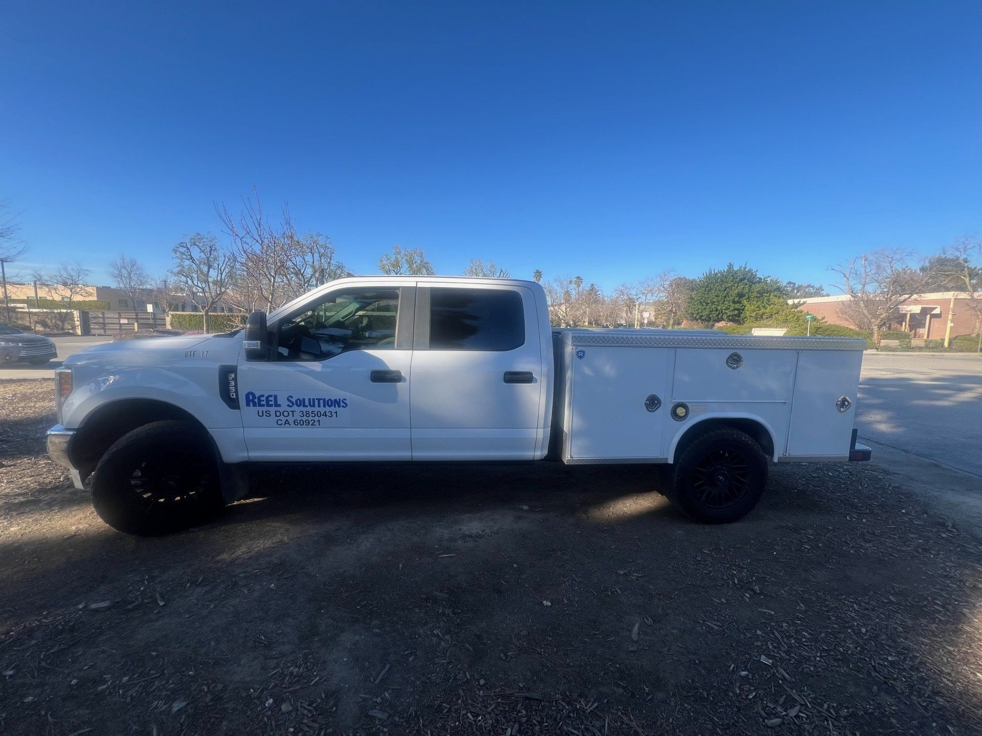 White Ford pickup truck with tool boxes parked on gravel.
