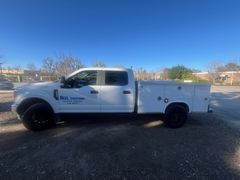 White Ford pickup truck with tool boxes parked on gravel.