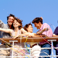 Four smiling people on a boat, surrounded by colorful streamers under a blue sky.