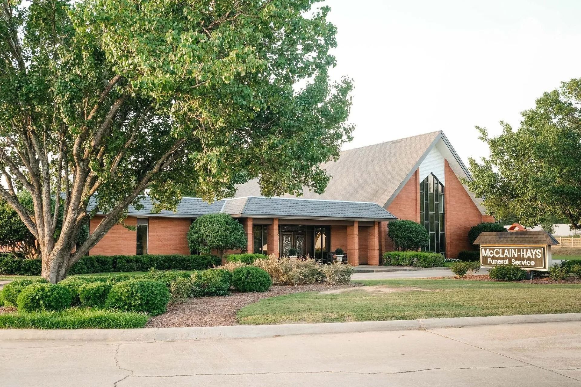 Red brick church building with trees and a sign.