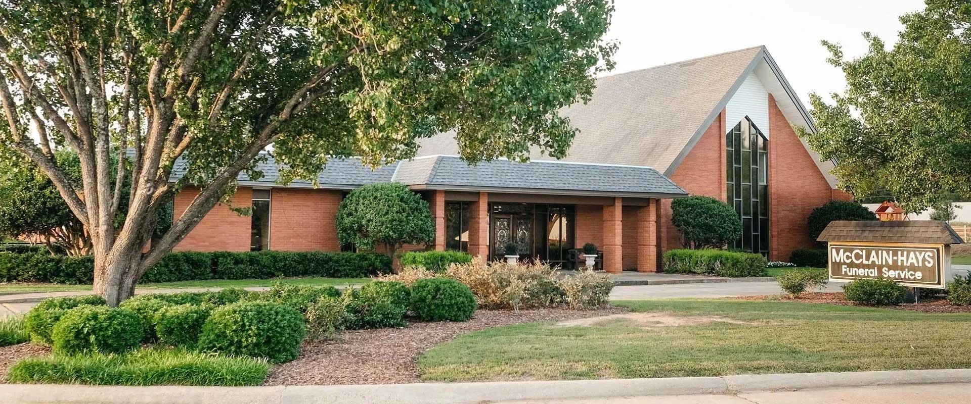 Exterior of a brick church with a sign in front, surrounded by trees and landscaping.