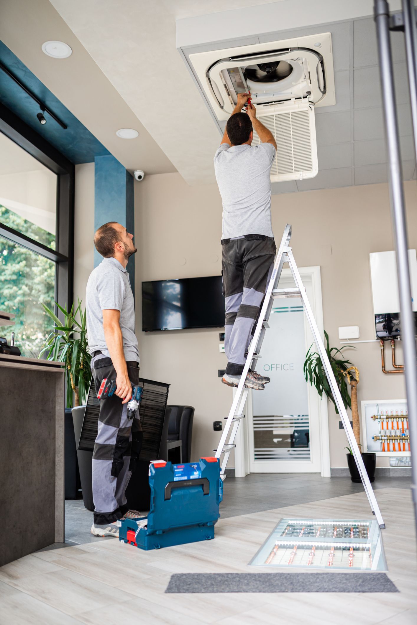 Two men are working on a ceiling fan in a room.