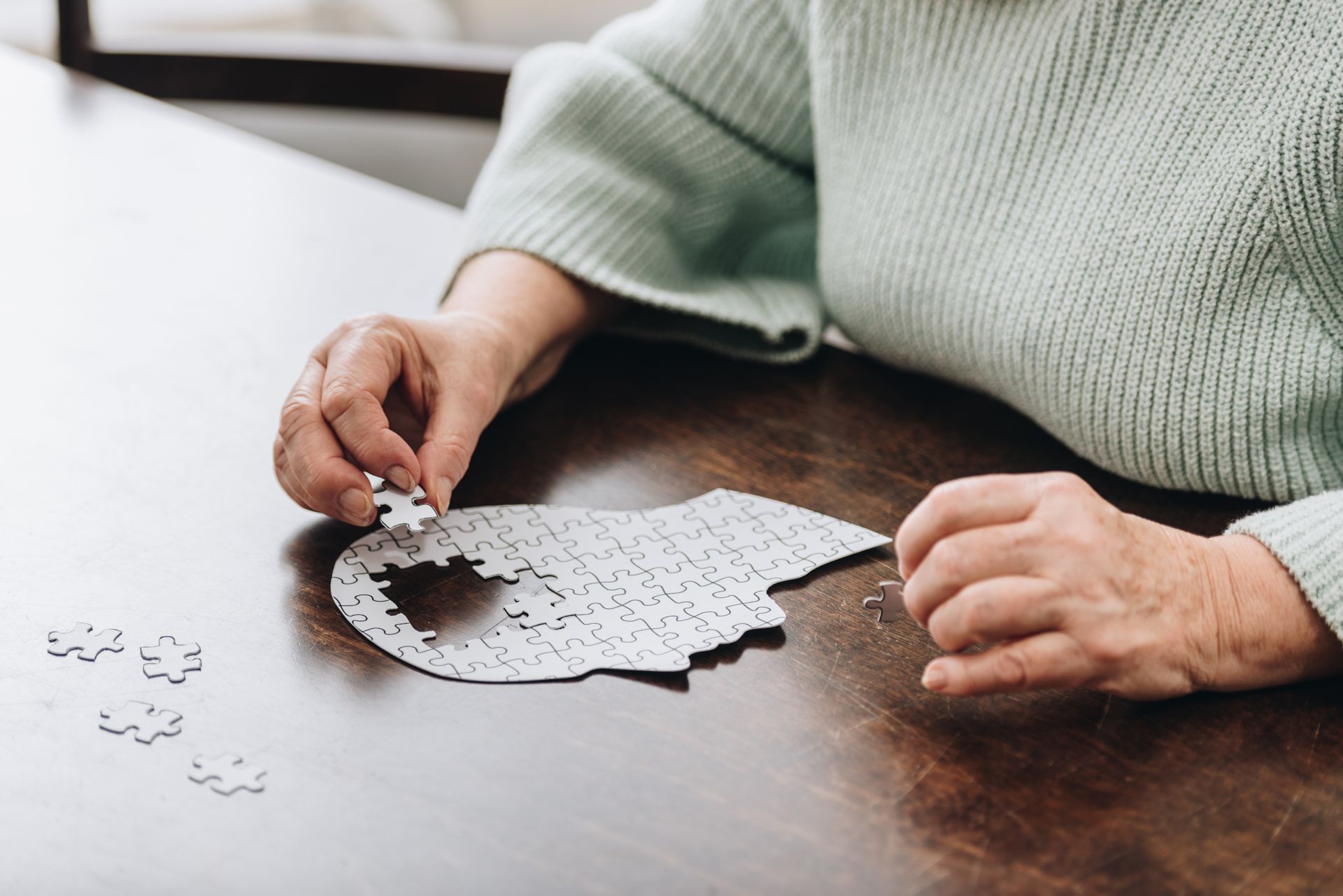 Person with hands assembling a brain-shaped jigsaw puzzle on a wooden table.