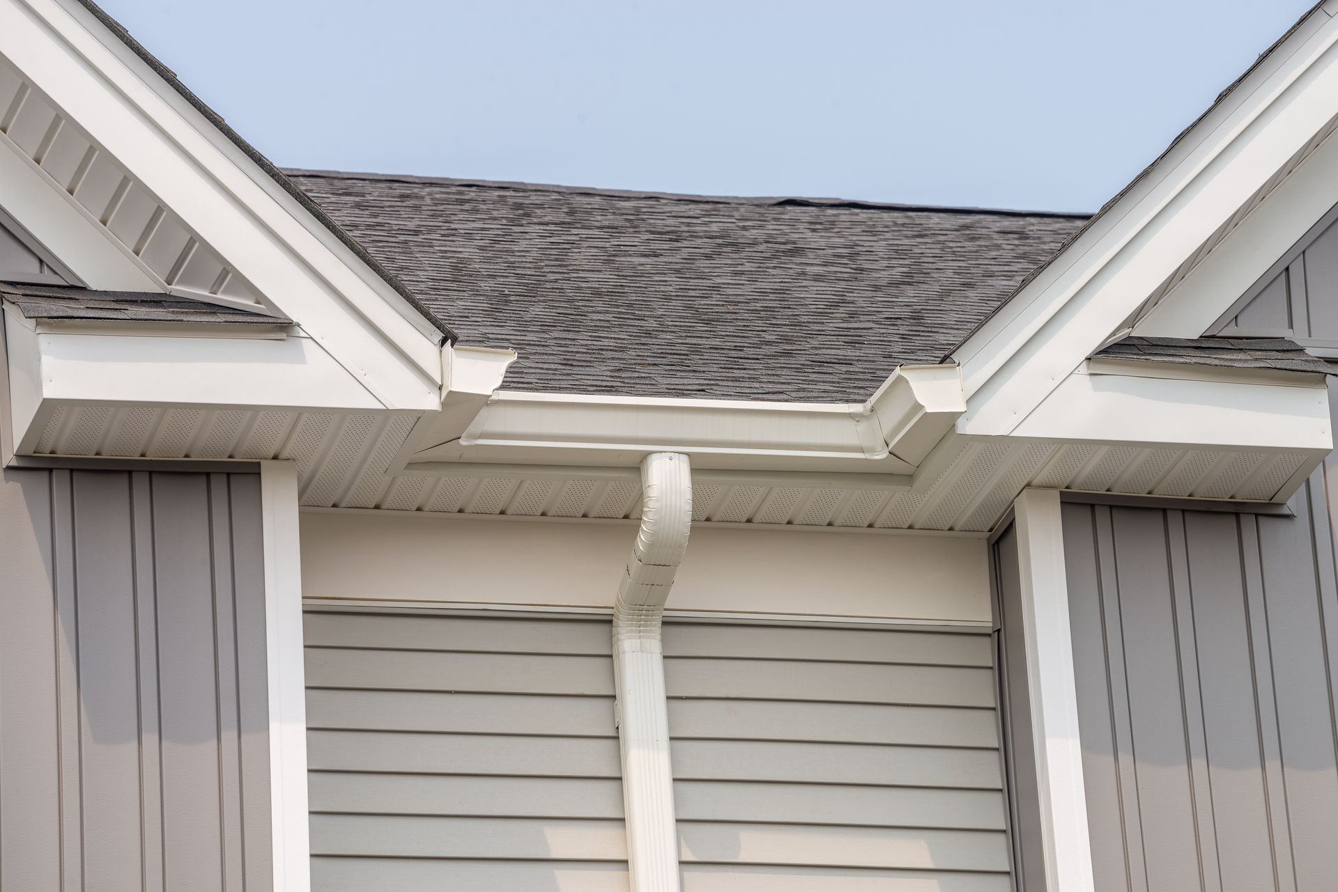 House roof with white trim, gray shingles, and a white downspout above closed shutters