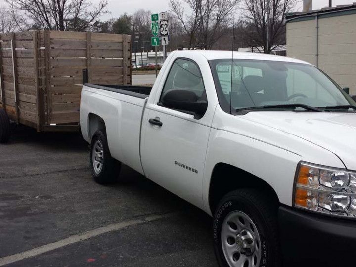 Woman in straw hat smiles, holding wine glass near a lake.