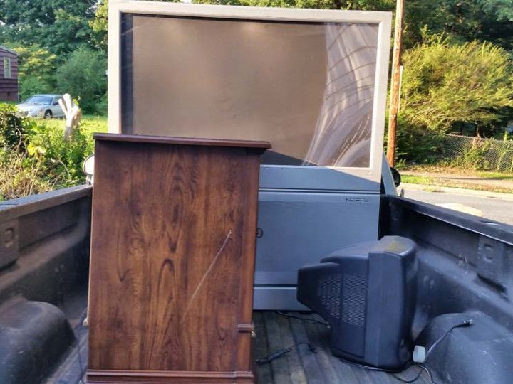 Woman in straw hat smiles, holding wine glass near a lake.