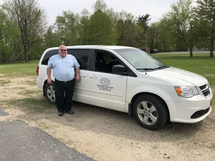 A man is standing next to a white van in a parking lot.