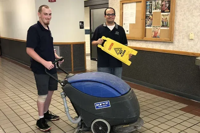 Two men are cleaning a floor with a machine.