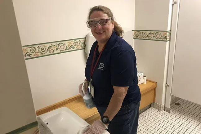 A woman wearing goggles is standing in a bathroom next to a toilet.