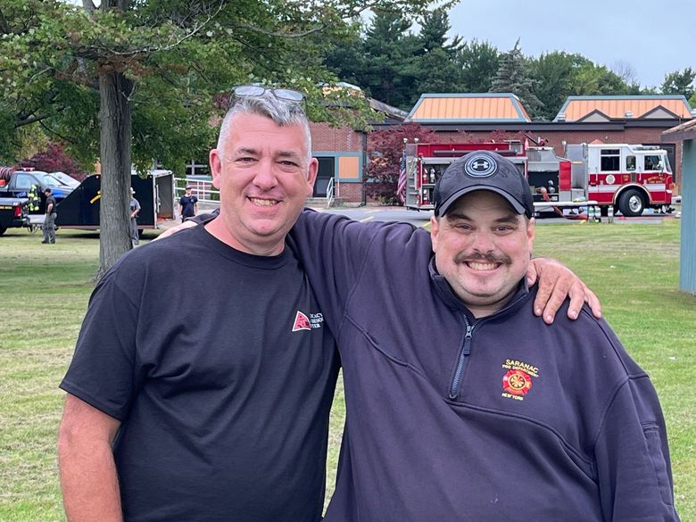 Two men are posing for a picture in front of a fire truck.