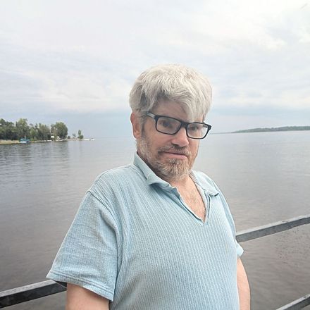 A man with glasses and a beard is standing next to a body of water.