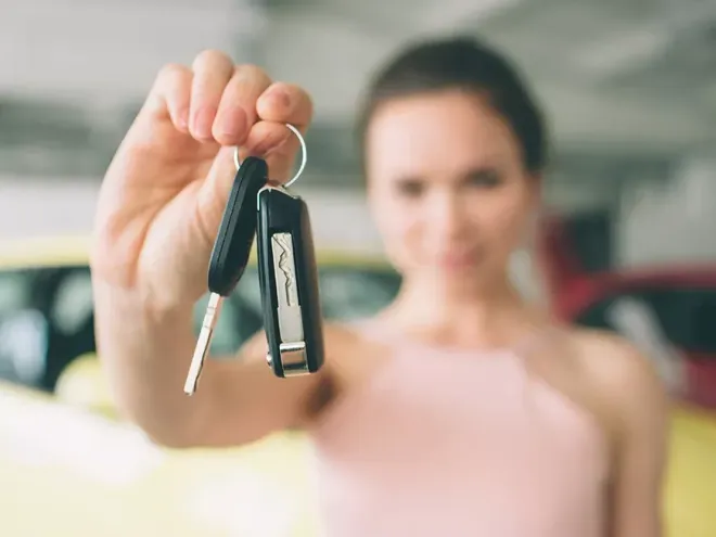 A woman is holding a pair of car keys in front of a yellow car.