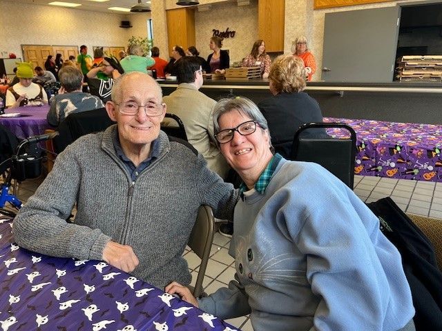 A man and a woman are posing for a picture while sitting at a table.