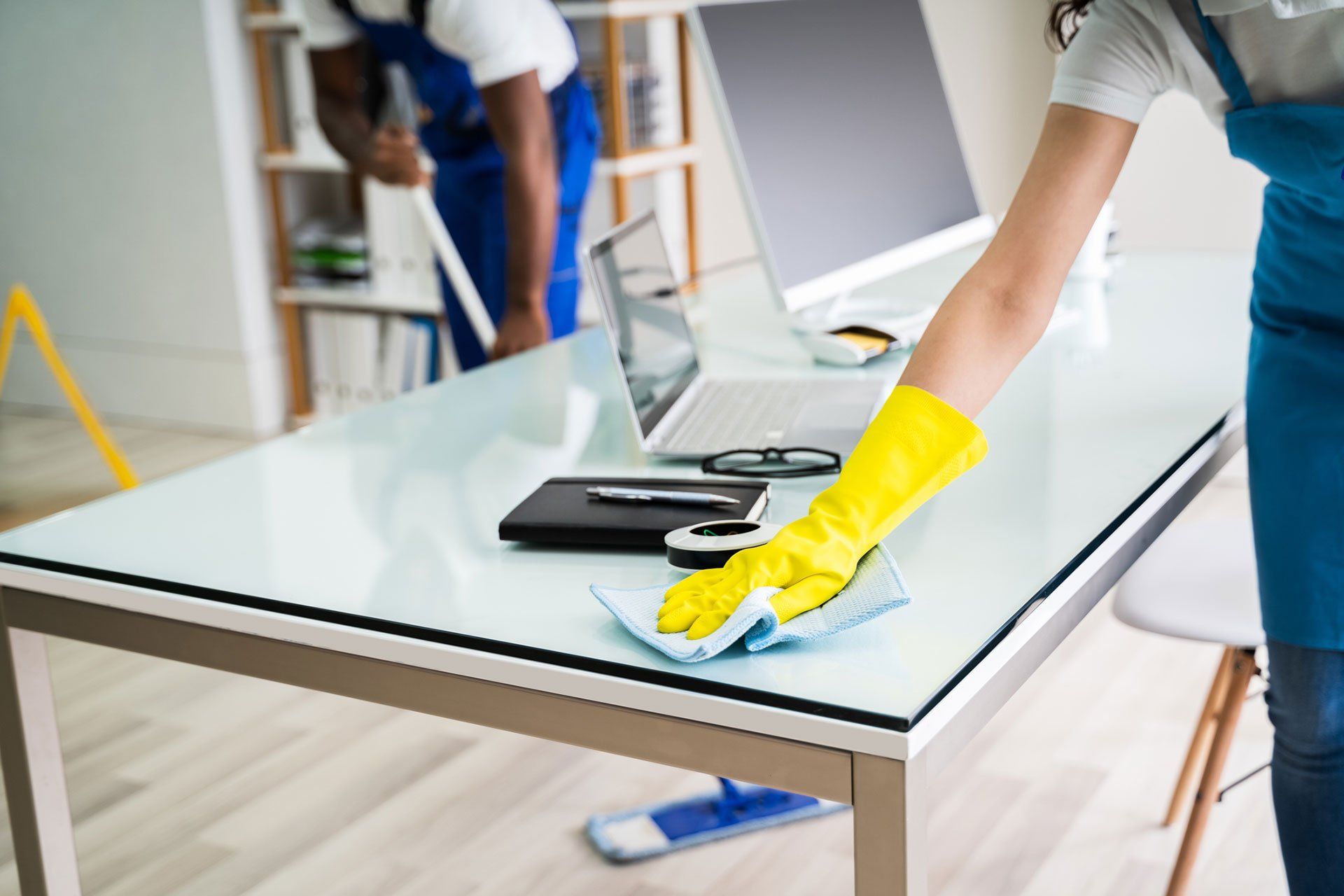 A woman wearing yellow gloves is cleaning a desk