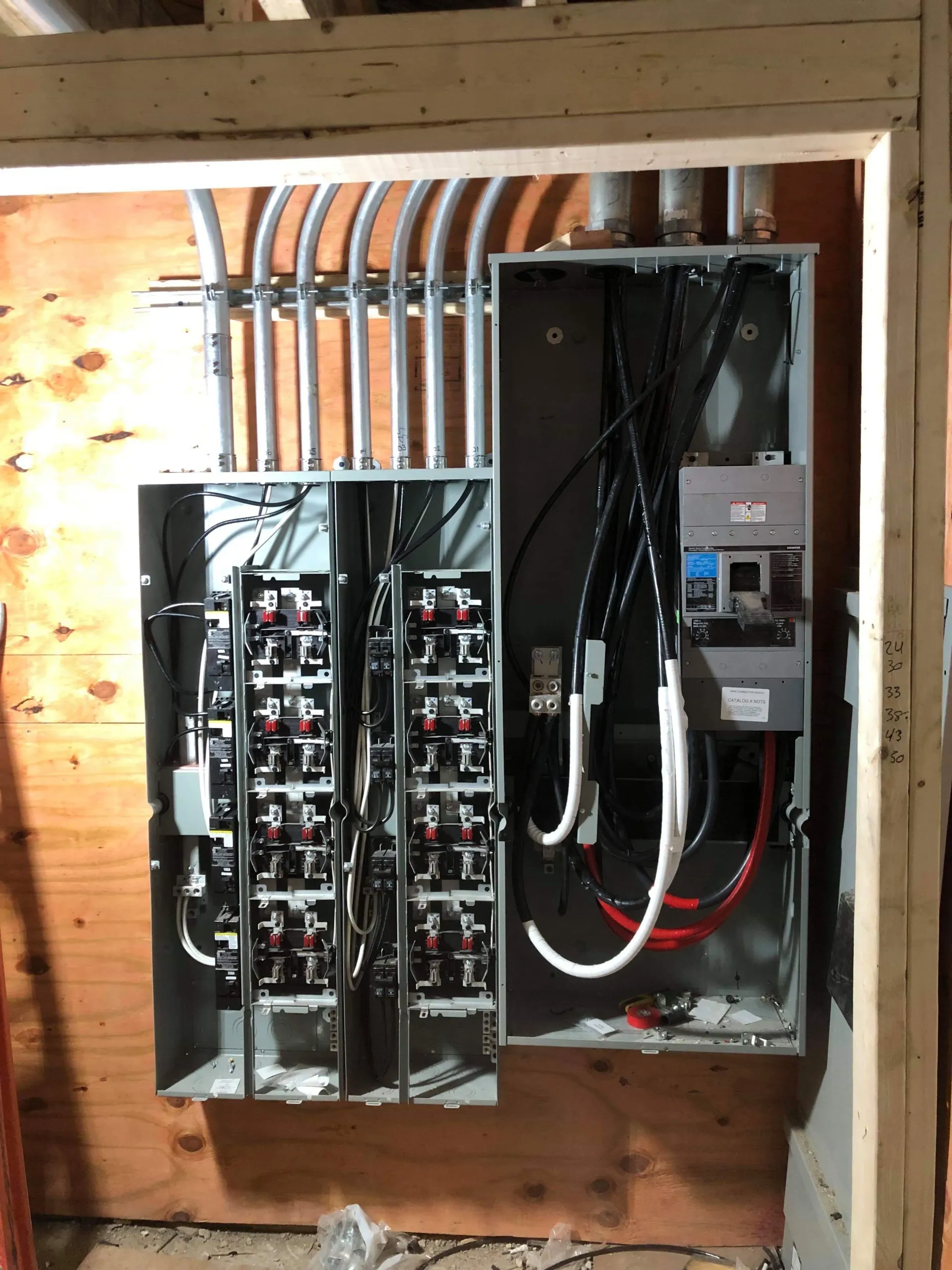 Electrical panel with conduit and wires on wooden wall.