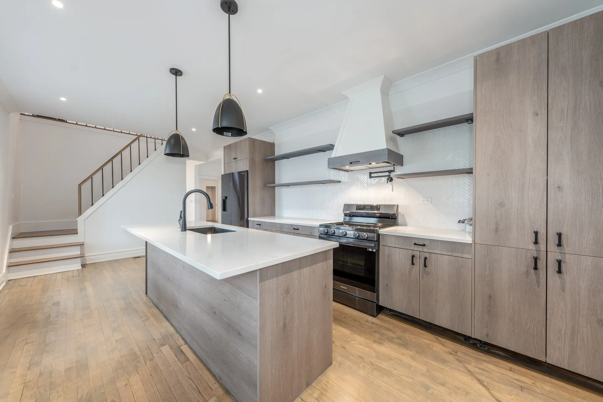 Modern kitchen with light wood cabinets, white countertops, and black pendant lights.