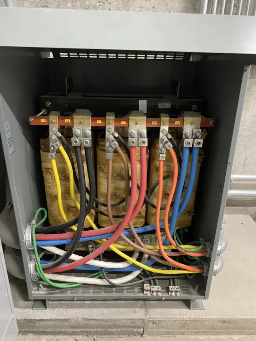Electrical transformer with color-coded wires in a metal enclosure.