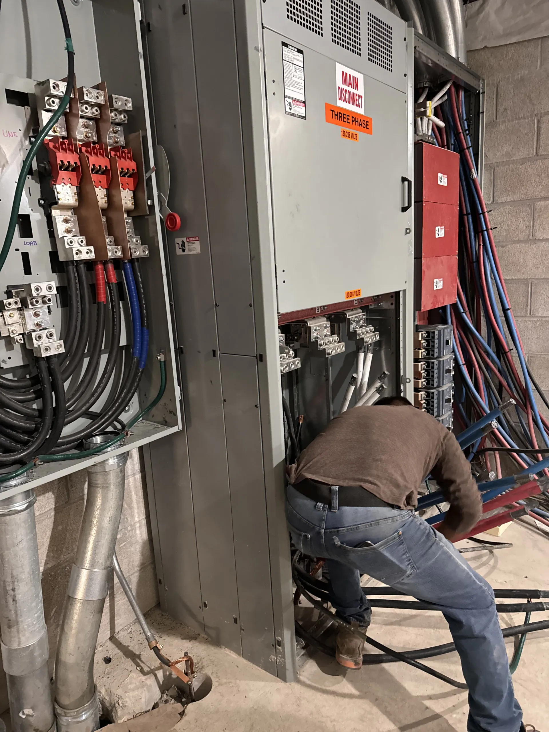 Electrician working on a large electrical panel with exposed wires in a construction setting.