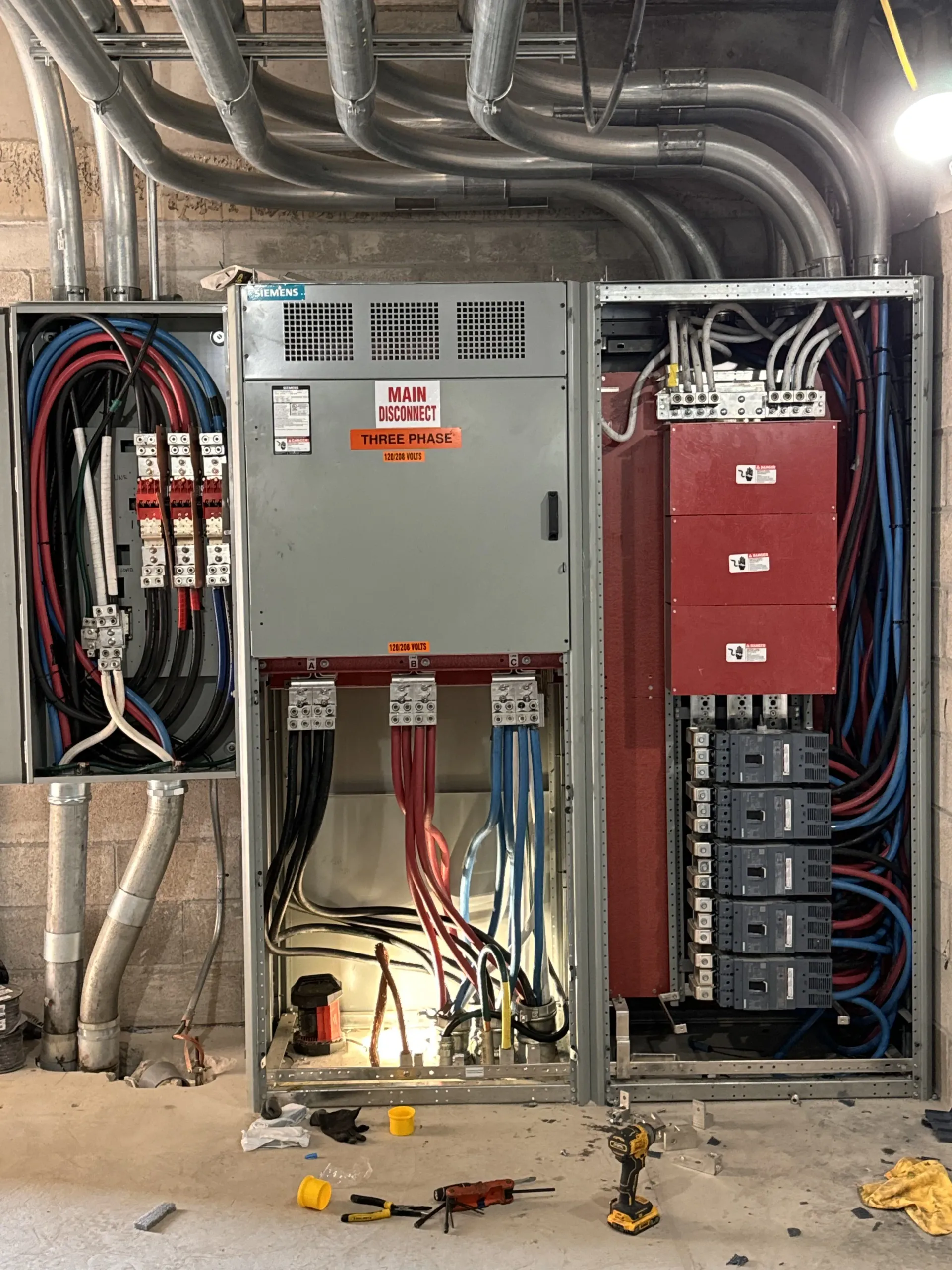 Electrical panel with colored wires and conduits in an unfinished construction site.