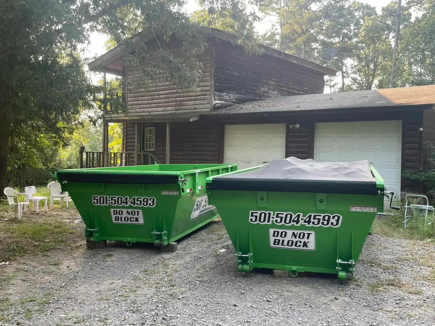 Two green dumpsters in front of a two-story log cabin with two garage doors, warning signs say
