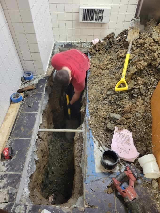 A man is digging a hole in the floor with a shovel.