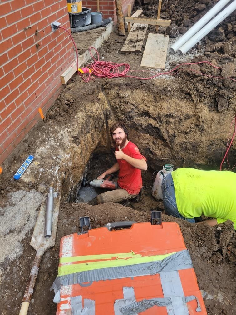 A man is kneeling in a hole in the ground giving a thumbs up.