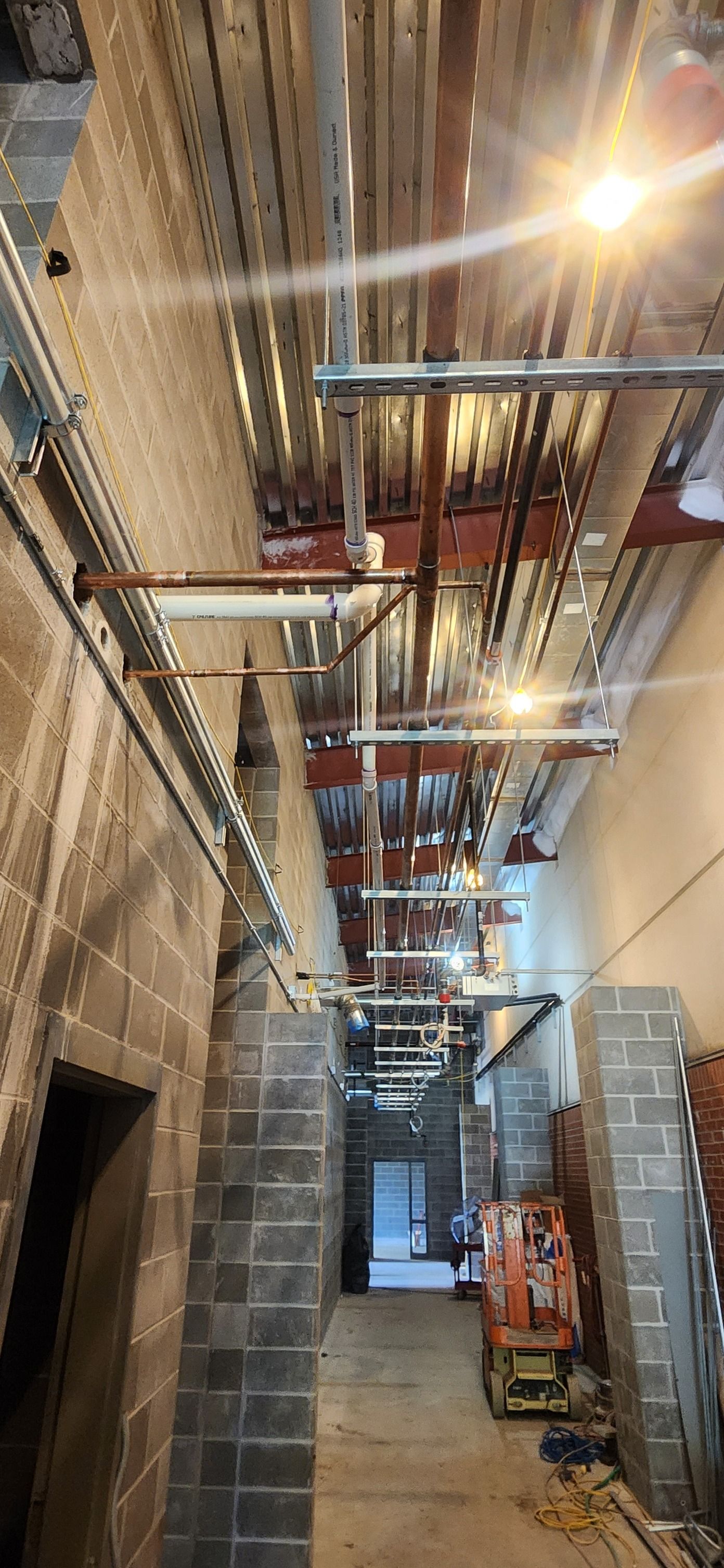 A long hallway with a lot of pipes hanging from the ceiling.