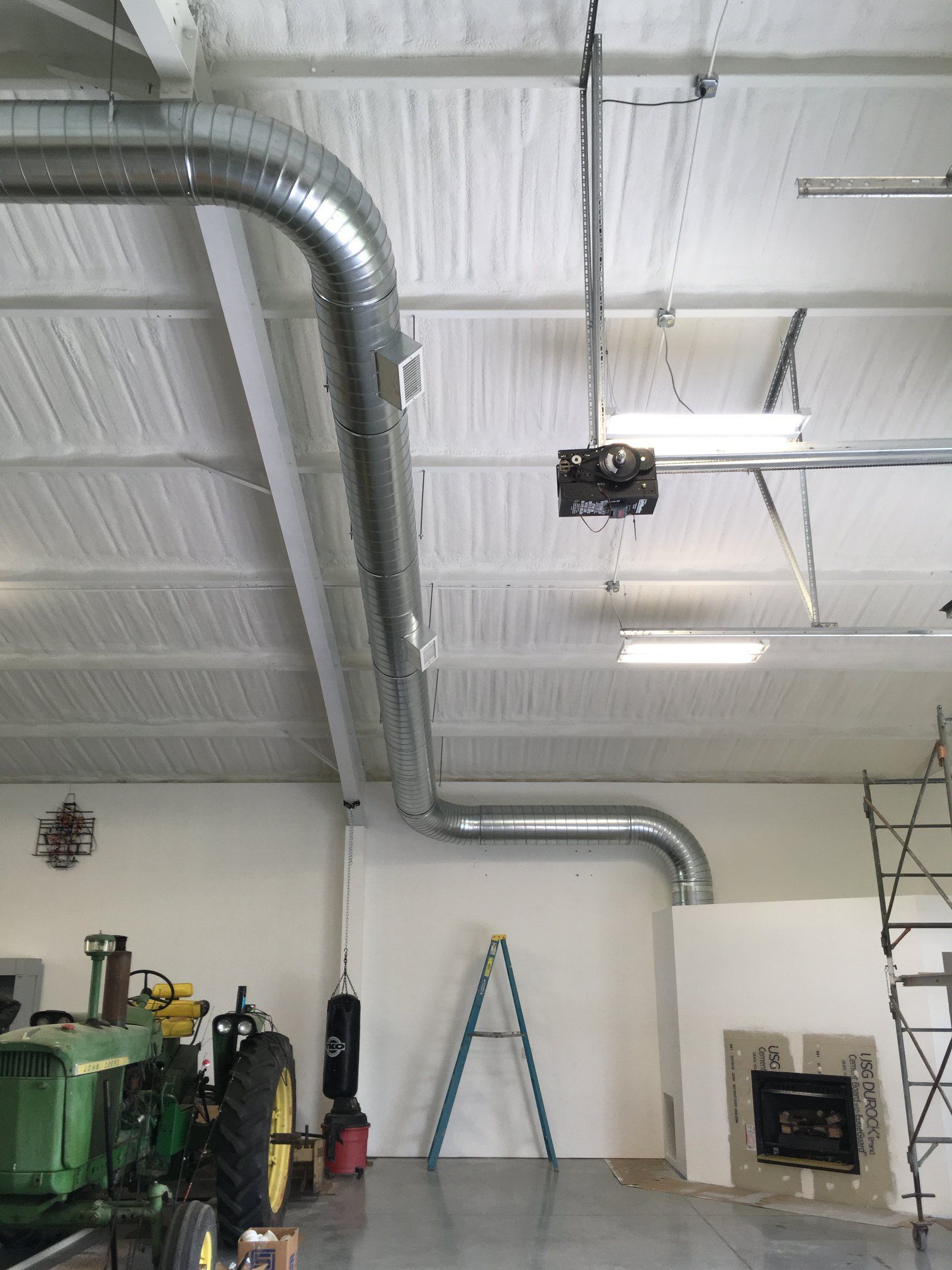 A john deere tractor is parked in a garage next to a ladder.