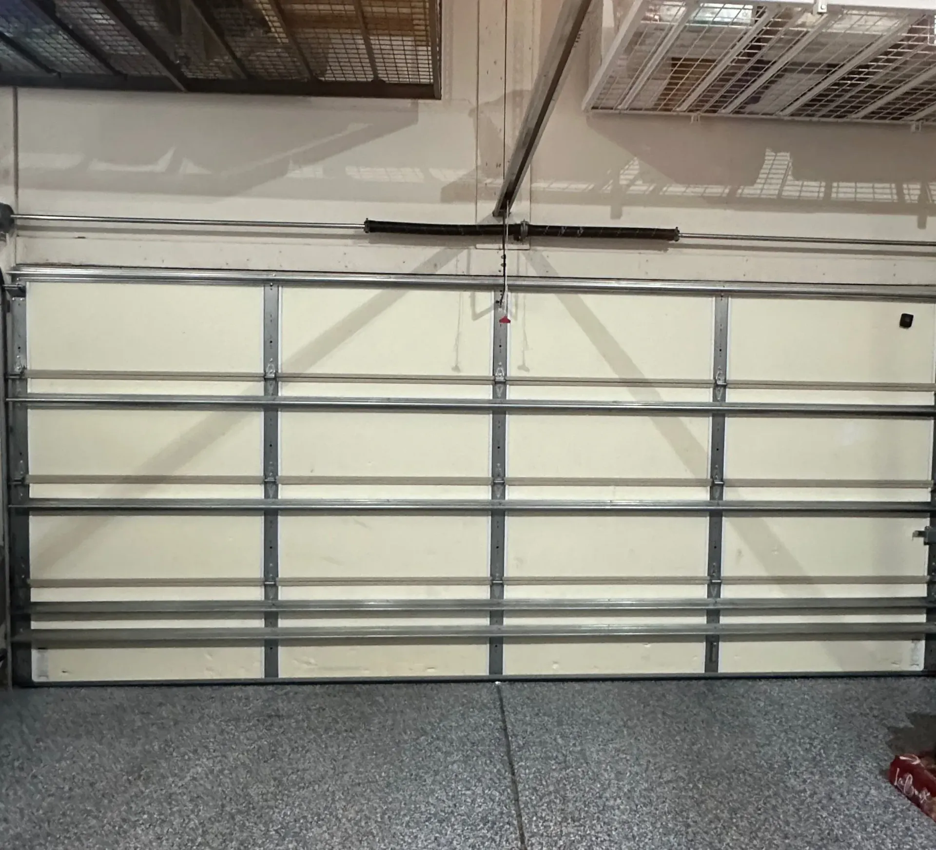 Garage door, tan panels, gray metal frame, overhead opener, inside a garage.