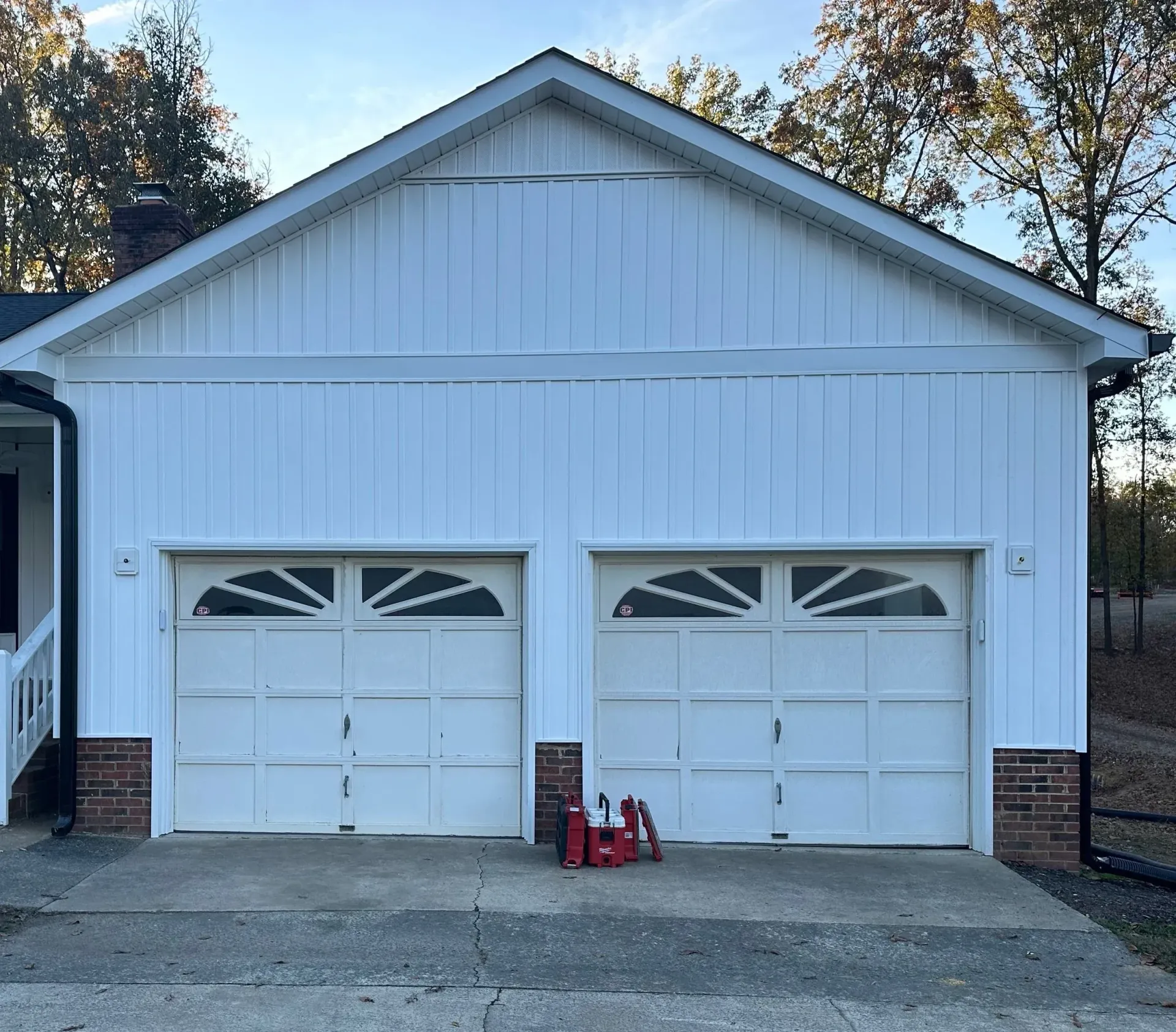 White two-car garage with arched windowed doors, brick accents, and a concrete driveway.