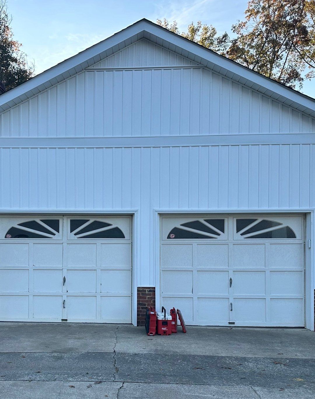 White two-car garage with arched windowed doors; tools and equipment in front.